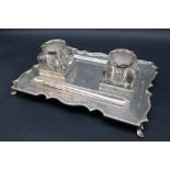 A George V silver desk standish, of rectangular form with a shaped border on four legs,