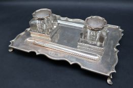 A George V silver desk standish, of rectangular form with a shaped border on four legs,