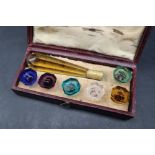 A 19th century cased set of six intaglio coloured-glass seals, with a faceted amber glass handle,