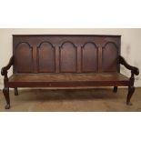 An 18th century oak settle with a five arched panel back and solid seat on cabriole legs and