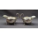 A pair of George V silver sauce boats with a gadrooned edge and scrolling handle on three legs with