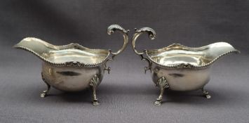 A pair of George V silver sauce boats with a gadrooned edge and scrolling handle on three legs with