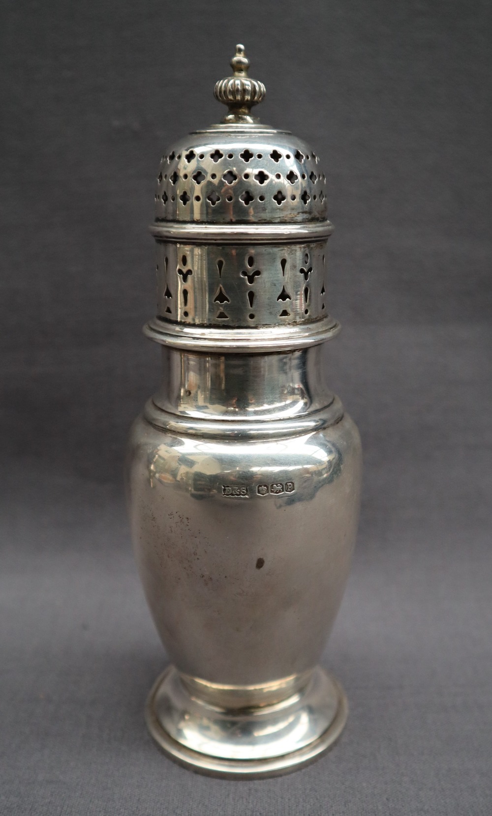 A George V silver sugar caster with a turned domed cover above a baluster body on a spreading foot,