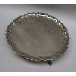 A George V silver salver of circular form with a shaped edge, on three legs and pad feet, London,