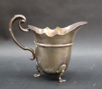 A late Victorian silver cream jug with a flared rim and scrolling handle on three feet, London,