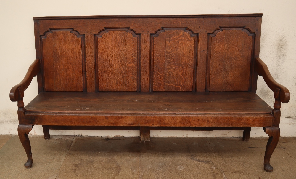An 18th century oak settle with a four panel back and solid seat on cabriole legs and pointed pad