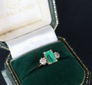 An 18ct gold emerald and diamond ring set with a central emerald approximately 9mm x 6mm flanked by