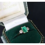 An 18ct gold emerald and diamond ring set with a central emerald approximately 9mm x 6mm flanked by