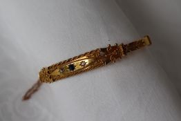 A 15ct yellow gold hinged bangle set with a central sapphire and two diamonds to a wire work and
