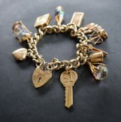 A 9ct yellow gold charm bracelet with a padlock clasp set with numerous charms including a heart