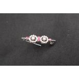 An 18ct white gold diamond and ruby bar brooch set with round brilliant cut diamonds in two floral