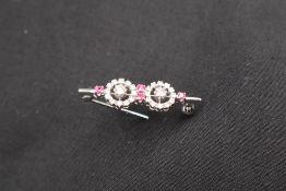 An 18ct white gold diamond and ruby bar brooch set with round brilliant cut diamonds in two floral