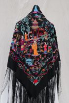 A black silk piano shawl with repeat hand embroidered design of figures in traditional dress