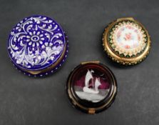 A blue enamel pill box and cover of circular form decorated with white flower heads and leaves to a