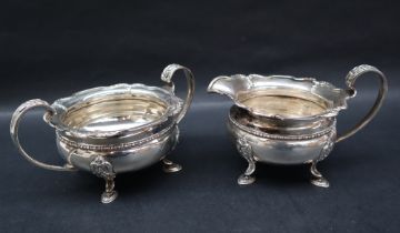 A George V silver cream jug and matching twin handled sugar basin, with a shaped leaf cast edge,