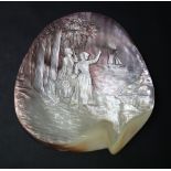 A shell carved with two female figures standing on the shore amongst trees waving to a boat at sea,