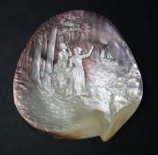 A shell carved with two female figures standing on the shore amongst trees waving to a boat at sea,