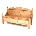 A pine settle, with shaped pediment over a single panel back, the solid seat with full width cover