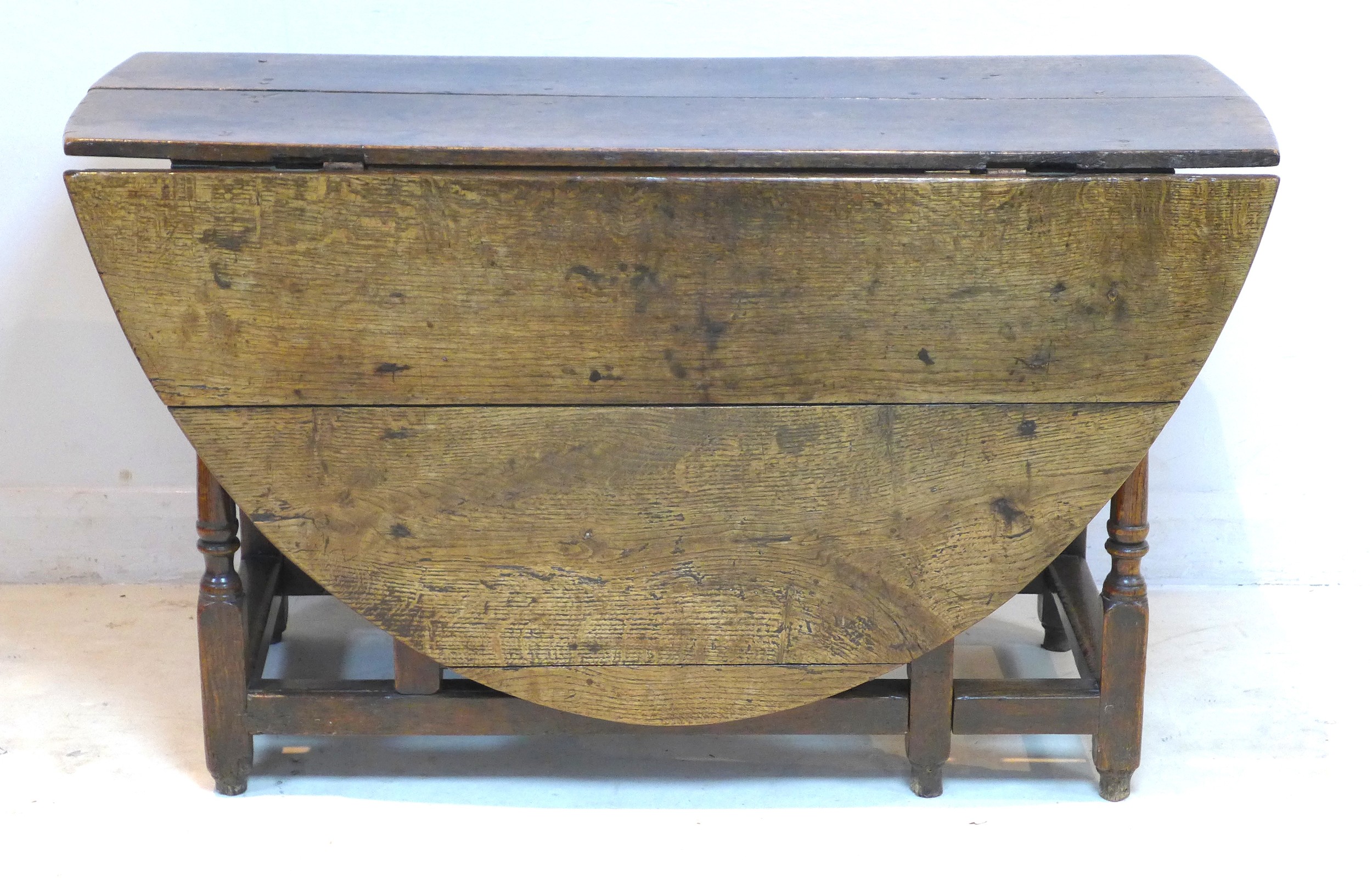 A 17th or 18th century oak drop leaf dining table, with oval surface, twin gate leg action, raised