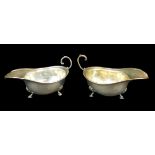 A pair of George V silver sauce boats, with reeded and foliate borders, raised upon tripod bases