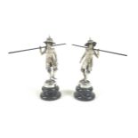 A pair of Burmese silver figures, in traditional dress, holding large poles, raised on circular