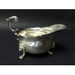 An Victorian silver sauce boat, with scroll handle, scalloped top rim and raised upon three lion