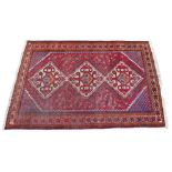 A Persian rug with red ground, three diamond medallions with white latchhook borders, orange, white,