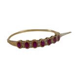A 9ct gold and ruby hinged bangle, set with seven oval cut rubies, in claw setting, interspersed