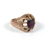 A 9ct gold and ruby coloured stone ring, the cushion cut stone 5 by 6.5mm, engraved scrolling leaves