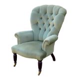 An Edwardian button back armchair, with green velvet upholstery, turned front legs and brass