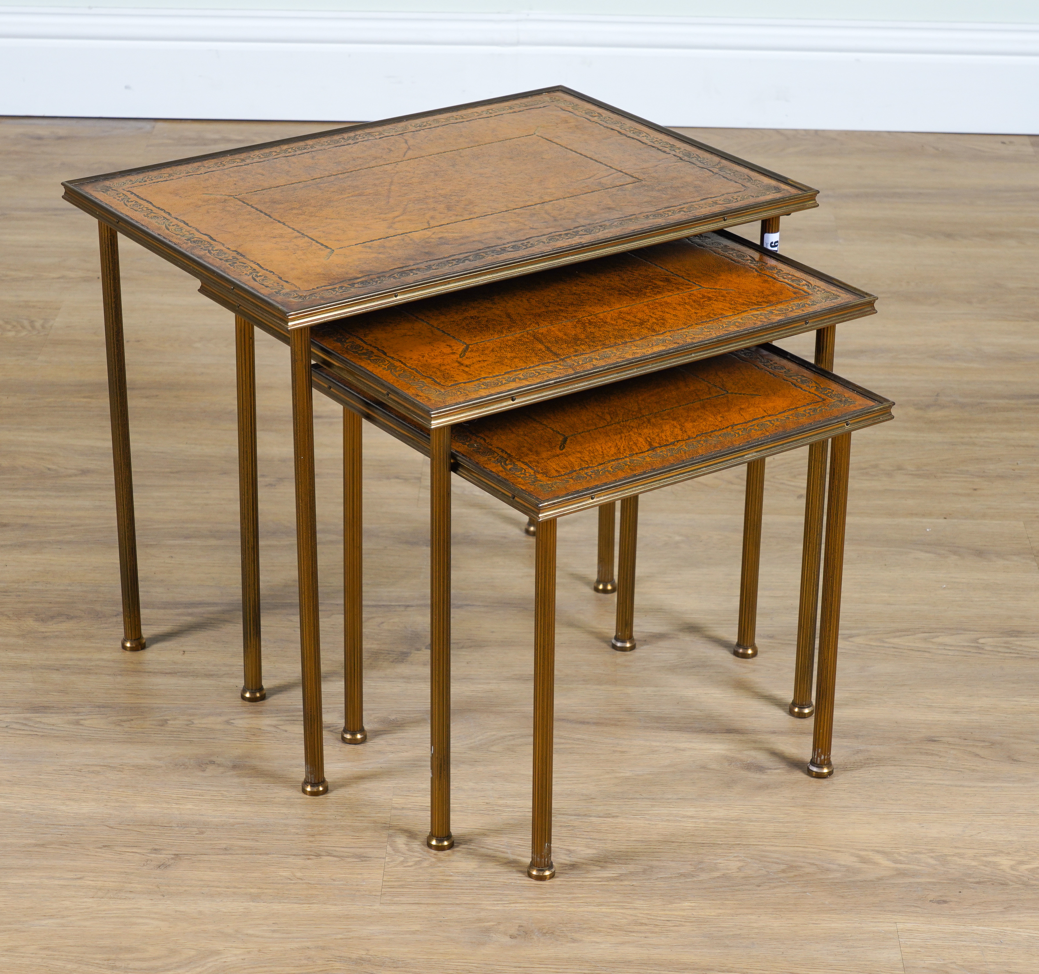 A NEST OF THREE MID-20TH CENTURY LEATHER INSET LACQUERED BRASS OCCASIONAL TABLES (3)
