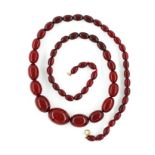 A SINGLE ROW NECKLACE OF GRADUATED OVAL SIMULATED CHERRY COLOURED AMBER BEADS