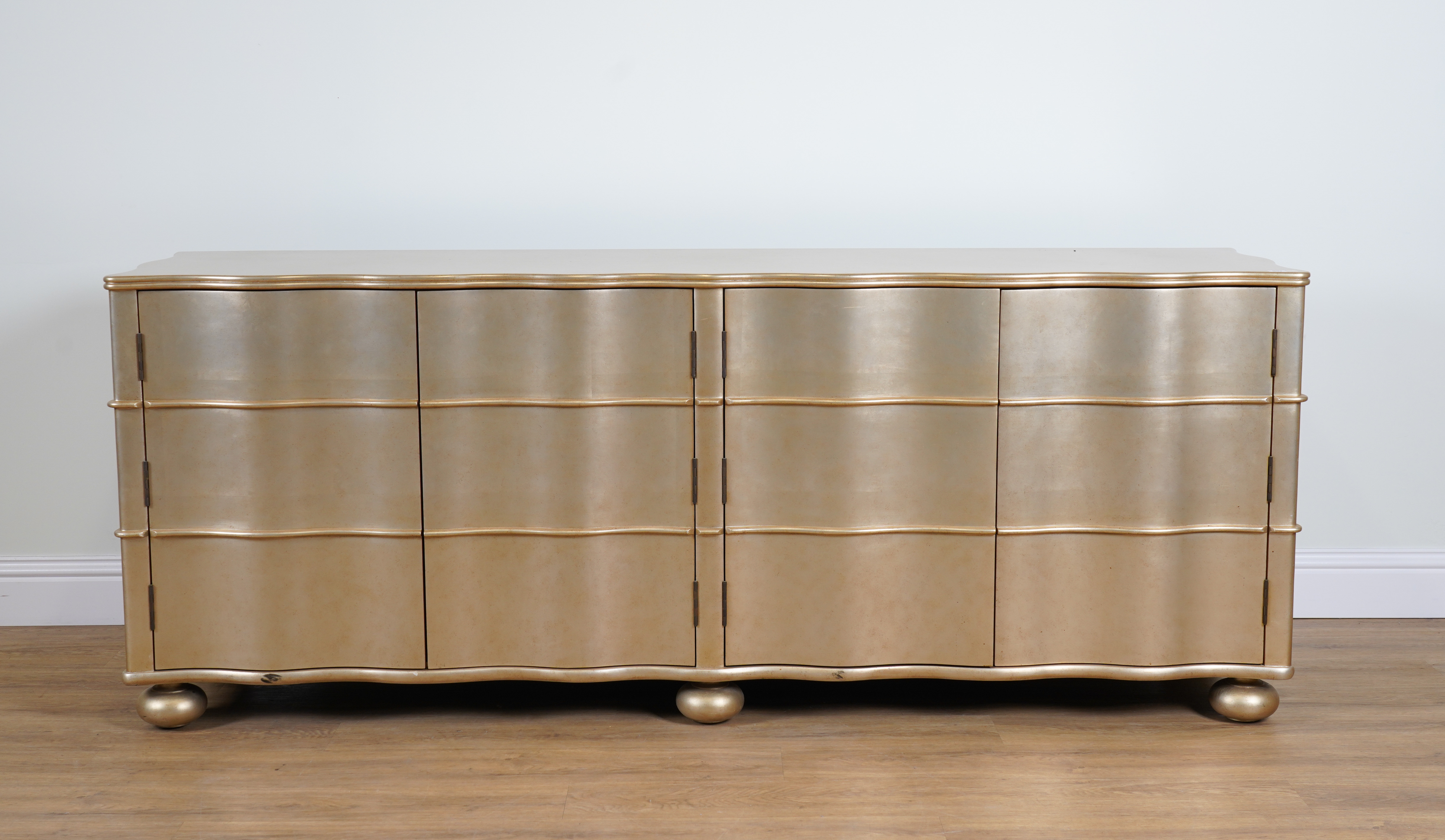 PAUL MARTIN; A GOLD PAINTED WAVY FRONTED FOUR DOOR LOW CABINET