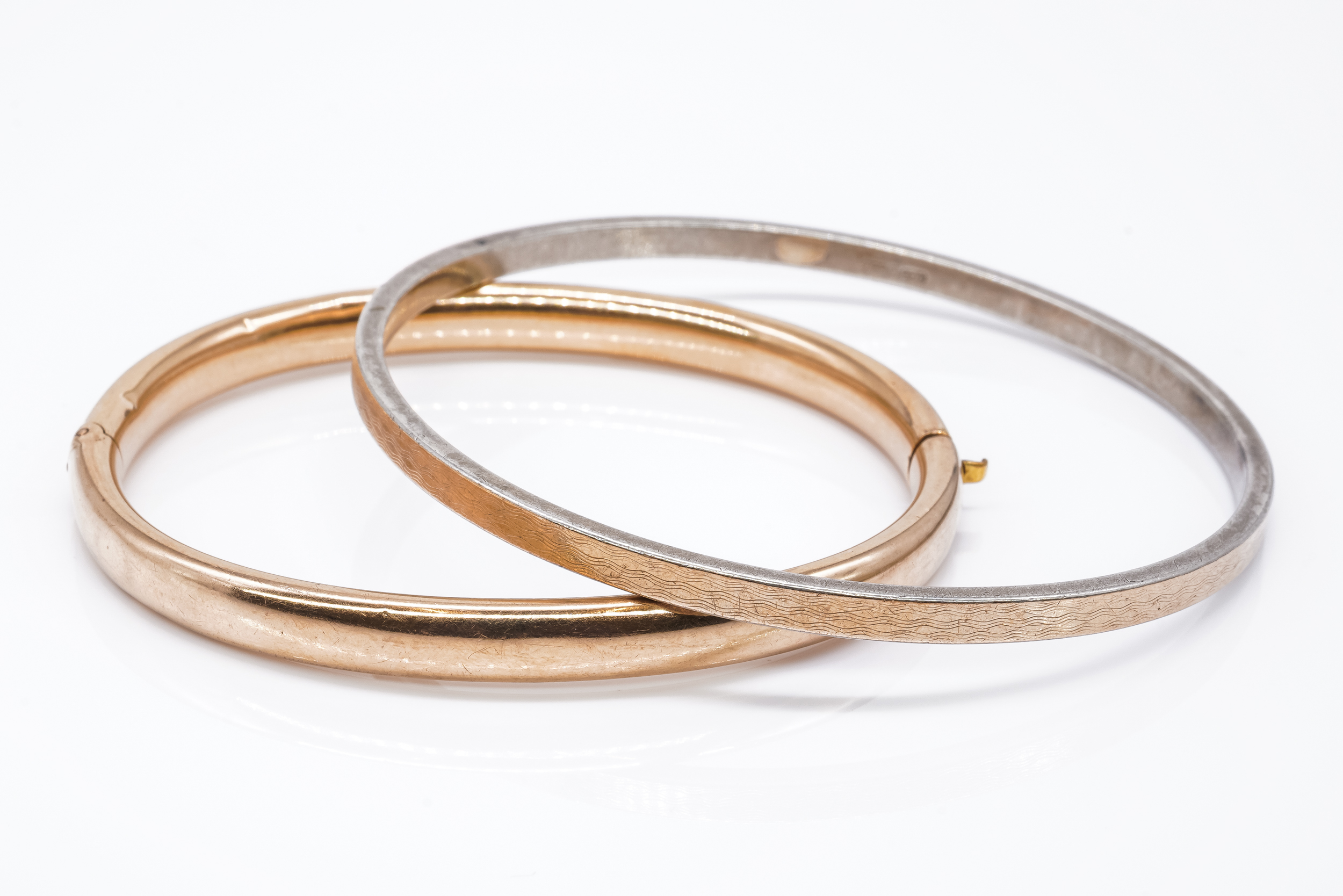 A GOLD HOLLOW OVAL HINGED BANGLE TOGETHER WITH A SILVER AND GOLD FRONTED CIRCULAR BANGLE (2)
