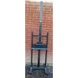 A vintage oak height adjustable artist’s easel, painted black, on splayed supports with castors.