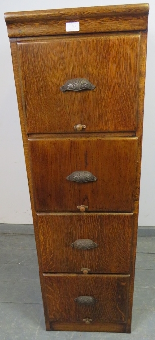 An early 20th century oak filing cabinet with fielded side panels, housing four drawers with cast