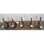 A row of five vintage cast iron and ceramic wall-hanging coat hooks on a hardwood mount with fielded