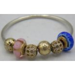 A Pandora white metal bangle with five 14ct gold beads, (2 with glass) charms, marked G585 ALE.