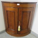 A George III mahogany bow fronted wall-hanging corner cupboard, with reeded edge, the panelled doors