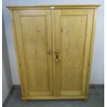 An antique stripped pine pantry cupboard, the panelled doors opening onto two fitted shelves, on bun