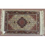 Small Persian rug, central red motif on beige ground within blue and red border fringe. 103cm x