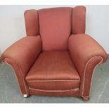 An Edwardian wingback club armchair, re-upholstered in light burgundy material with silver braided