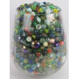 A large quantity of glass marbles of mixed size and colours, collected in a glass vase. Vase: 9.1 in