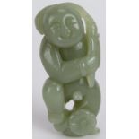A Chinese carved celadon Jade figure of a boy holding a branch above his head and standing on a