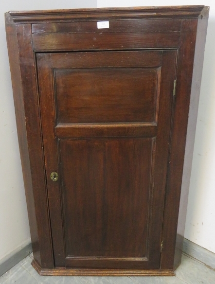 A Georgian oak wall-hanging corner cupboard, the panelled door opening onto three shaped shelves.