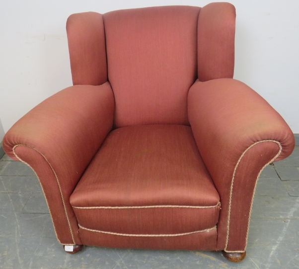 An Edwardian wingback club armchair, re-upholstered in light burgundy material with silver braided
