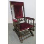 An Edwardian ebonised American style ‘Dexter’ rocking chair, upholstered in plum velvet material, on
