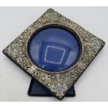 A square silver photograph frame heavily embossed with foliate design and with circular concave