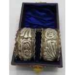 A pair of silver napkin rings heavily embossed with scrolls and foliate design, monogrammed,