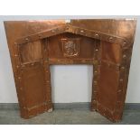 An Arts & Crafts copper fire surround with banded and riveted detail and repousse central crest